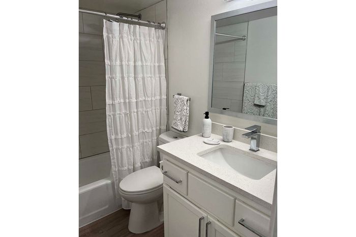 Elegant bathroom with modern fixtures, featuring a stylish vanity, pristine white shower curtain, and chic gray accents.