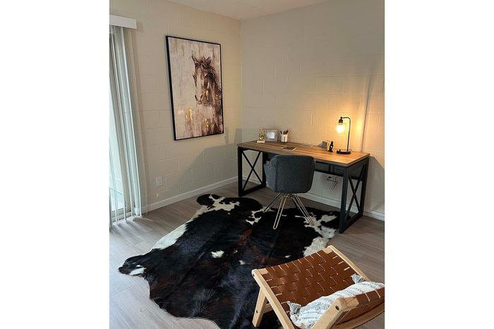 Inviting home office with a sleek wooden desk, comfortable chair, artistic horse painting, and warm lighting, accented by a stylish cowhide rug.