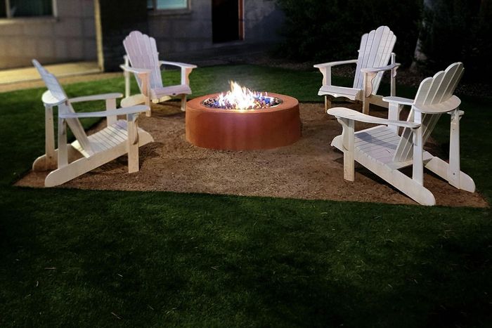 Inviting outdoor fire pit area with four Adirondack chairs, perfect for cozy evening gatherings on lush green lawn.