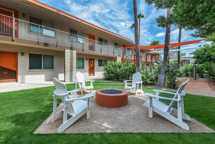 Welcoming apartment complex courtyard featuring a cozy fire pit with white Adirondack chairs, vibrant green lawn, and modern two-story buildings.