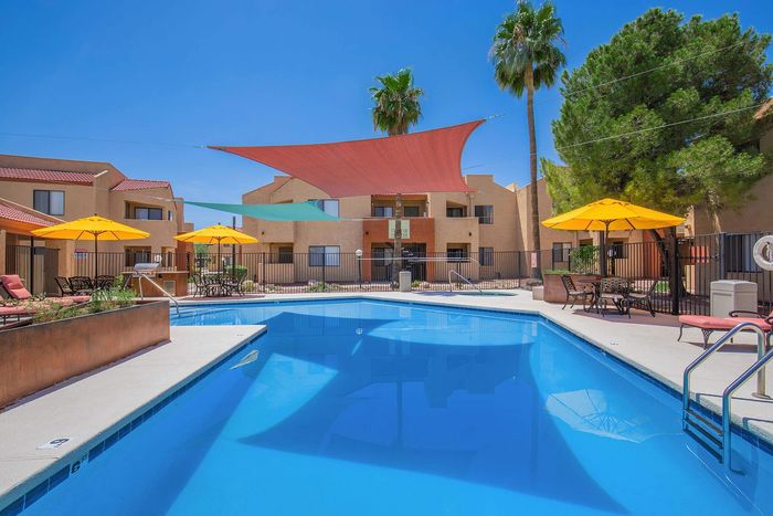 Vibrant apartment complex pool area featuring sparkling blue water, stylish loungers, and yellow umbrellas under a clear blue sky.