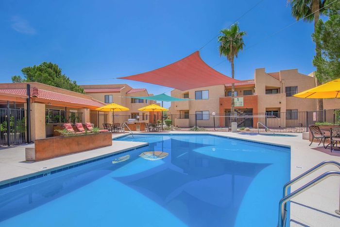 Inviting pool area with sun loungers and vibrant umbrellas at a modern apartment complex, perfect for relaxation and leisure.