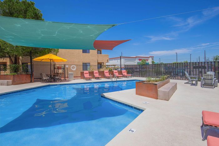 Inviting apartment complex swimming pool with vibrant lounge chairs, sunshade sails, and a cozy seating area for relaxation under the blue sky.