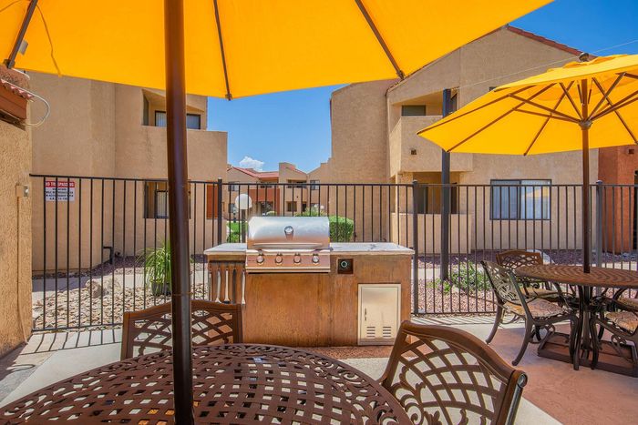 Charming outdoor dining area with a barbecue grill, shaded by vibrant yellow umbrellas, perfect for entertaining and relaxation in a sunny courtyard.