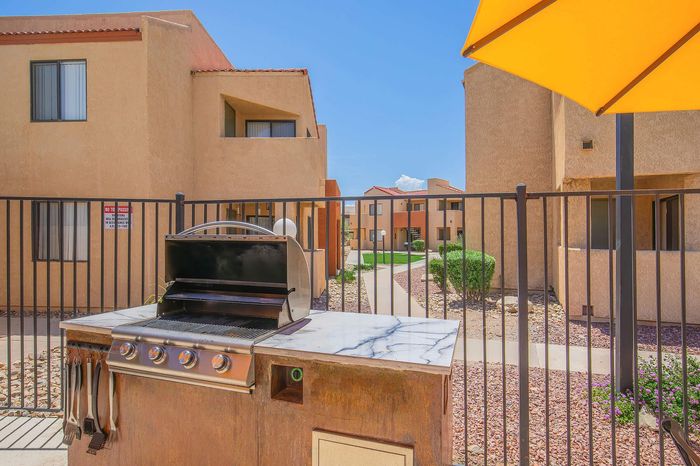 Inviting outdoor area with a modern BBQ grill, surrounded by charming desert-style apartment buildings and vibrant landscaping, perfect for entertaining under the sun.