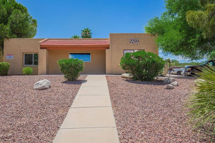 Charming desert-style home with a vibrant red-tiled roof, framed by lush greenery and picturesque blue sky.