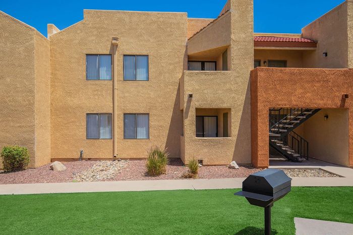 Charming apartment facade with textured walls, large windows, and inviting staircase entry, set in a beautifully landscaped courtyard with lush green grass and a barbecue grill.