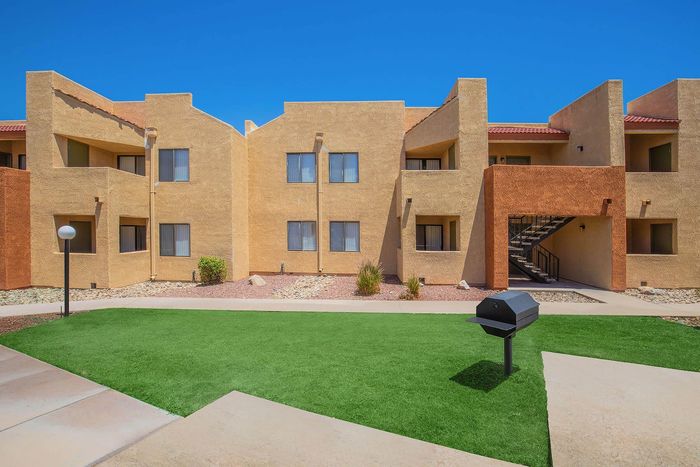 Vibrant apartment exterior with a modern architectural design, featuring earthy tones, manicured lawn, and a convenient outdoor grill area.
