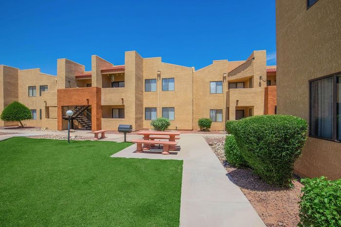 Modern apartment complex with beautiful landscaping, bright stucco exteriors, and a serene courtyard featuring picnic tables and lush greenery.