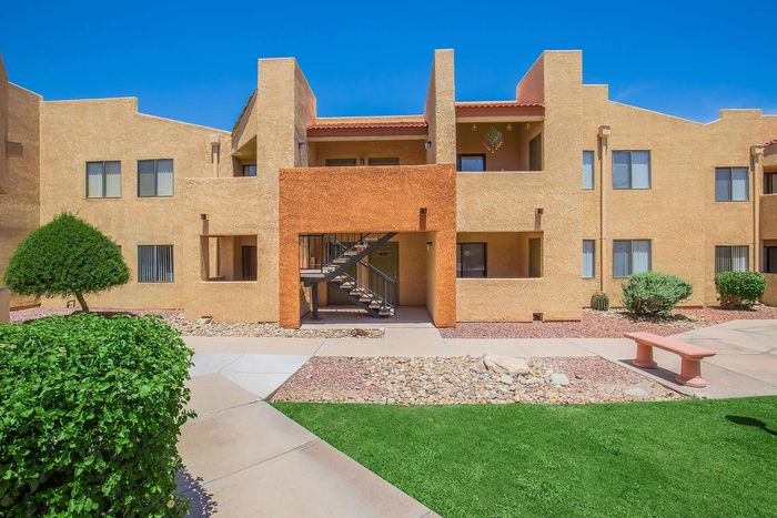 Charming apartment complex with vibrant stucco facade, manicured landscaping, and inviting pathways under a clear blue sky.