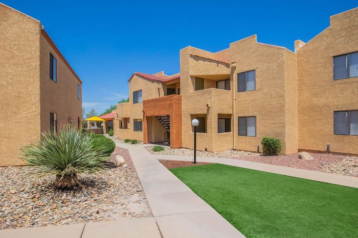 Charming desert-colored apartment building with lush landscaping and inviting pathways, under a bright blue sky.