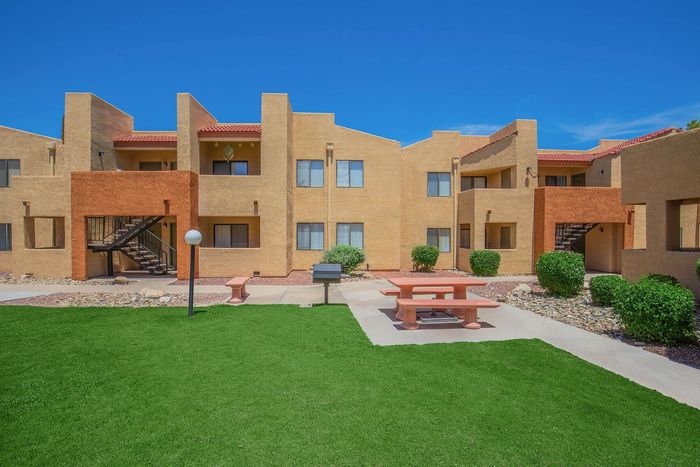 Charming apartment complex with vibrant architecture, lush green landscaping, and inviting outdoor seating area under a clear blue sky.