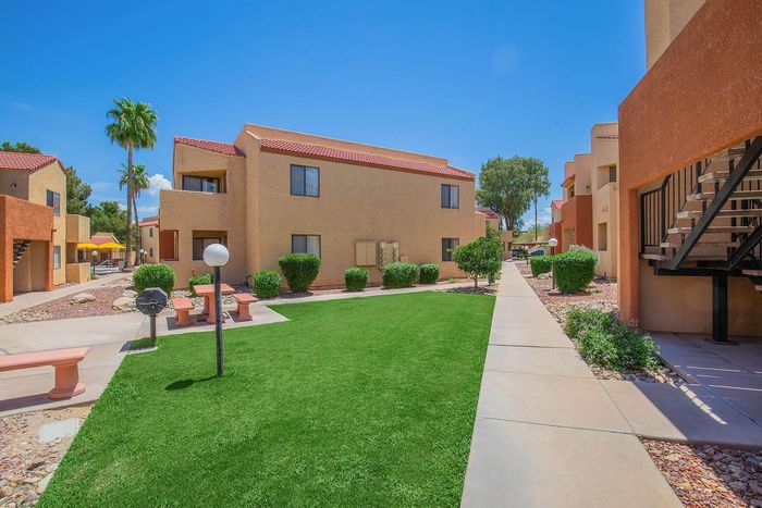Charming apartment complex with vibrant greenery, palm trees, and well-maintained pathways under a clear blue sky.