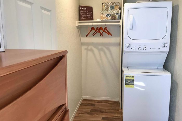 Cozy laundry nook with in-unit washer and dryer, modern wooden dresser, and hanging space in a bright, inviting apartment.