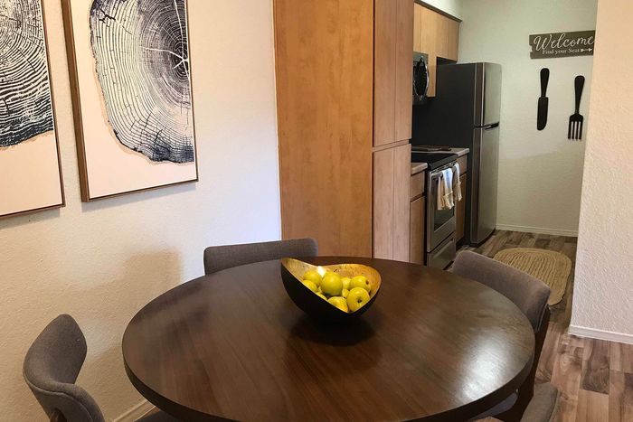Cozy dining area with a round wooden table, stylish gray chairs, and vibrant bowl of lemons, leading to a modern kitchen with stainless steel appliances.