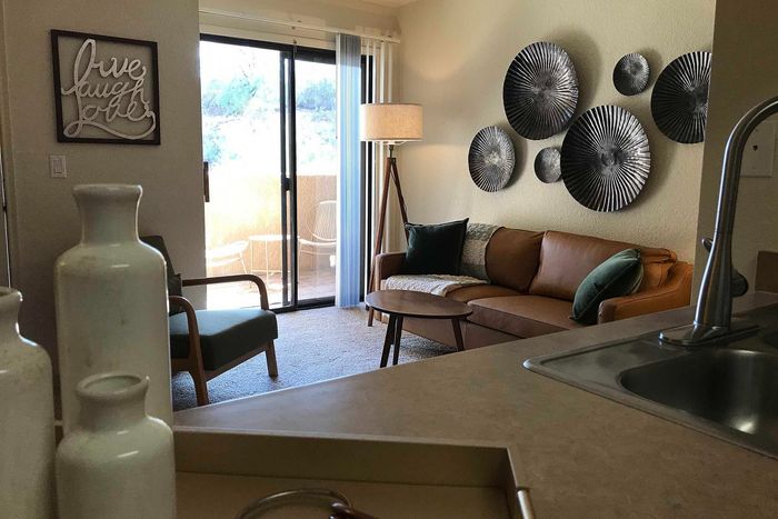 Inviting living room with contemporary decor, featuring a cozy brown sofa, eclectic wall art, and abundant natural light from a large sliding door opening to a serene balcony view.
