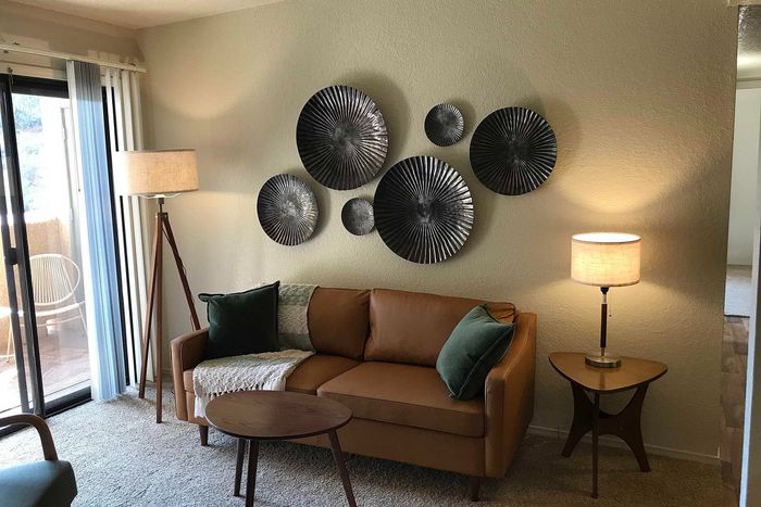 Cozy living room featuring a stylish tan sofa with green cushions, modern wall art, and a warm ambiance from soft lighting and natural light from the balcony.