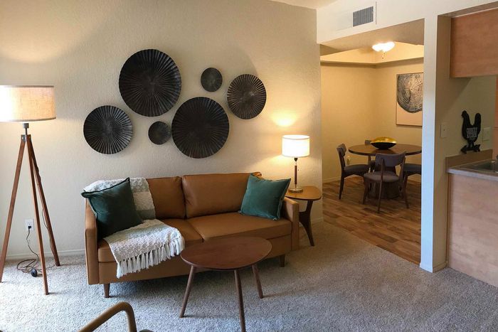 Cozy and stylish living room with a tan leather sofa, artistic wall d&eacute;cor, and ambient lighting leading to an inviting dining area.