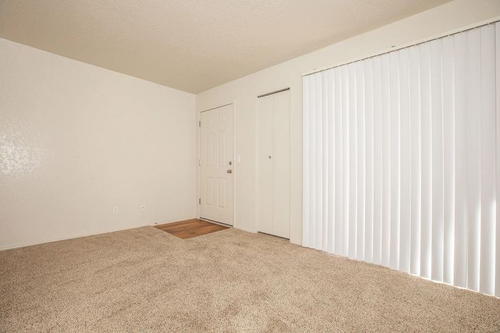 Spacious living area with plush carpet and vertical blinds offering plenty of natural light.