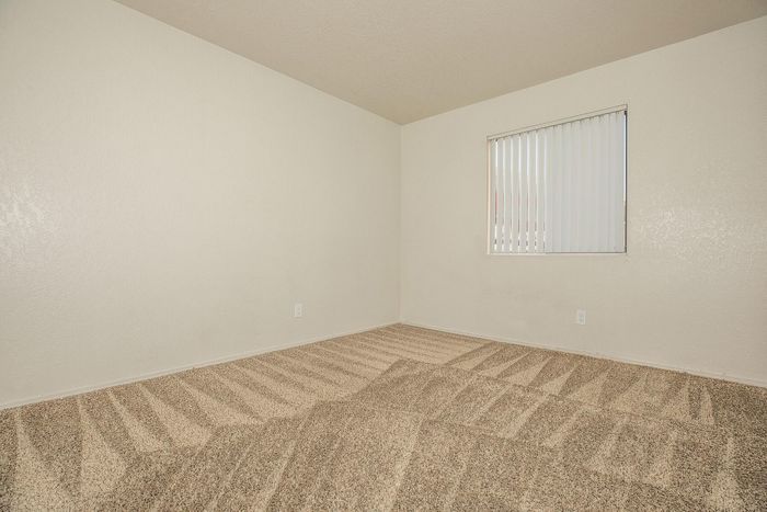 Bright, empty room featuring clean beige carpet and a window with vertical blinds.