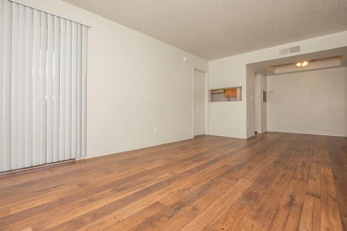 Bright, spacious living area with elegant wooden flooring and soft natural light through vertical blinds.