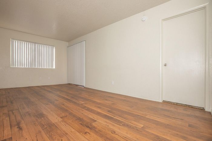 Bright and spacious room featuring elegant wooden flooring and vertical blinds, perfect for a cozy living space.