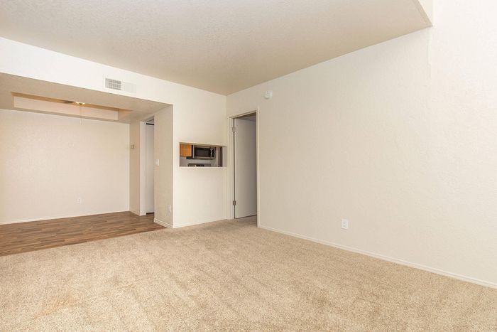 Bright and inviting living space with a mix of carpet and wood flooring, featuring a convenient pass-through from the kitchen and a modern layout.