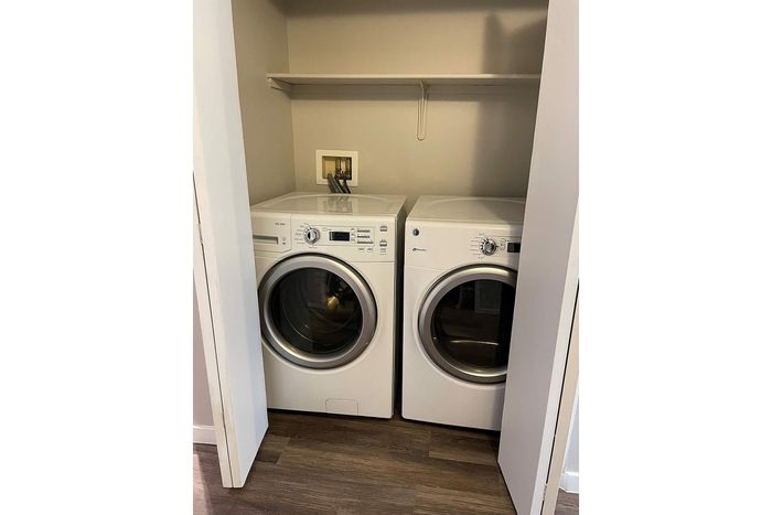 Modern laundry space with sleek washer and dryer set, enclosed in a compact closet with wooden flooring.