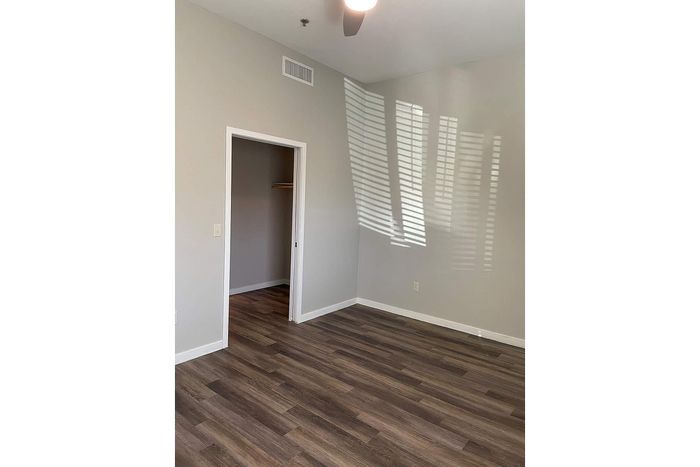 Modern bedroom with sleek hardwood floors, neutral gray walls, and a partially open closet space.