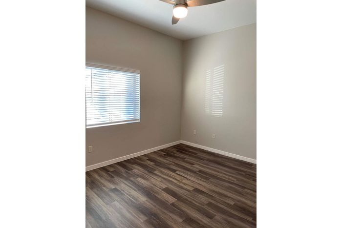 Sunlit room with sleek hardwood flooring and modern ceiling fan, featuring a large window with blinds.