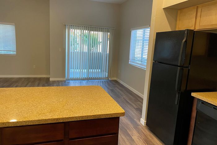 Modern apartment kitchen with sleek black appliances, granite countertops, and rich hardwood floors, bathed in natural light through large windows.