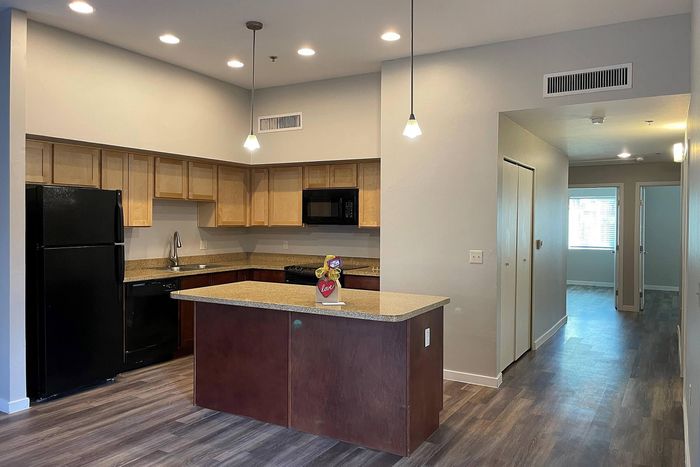 Modern kitchen with sleek black appliances, warm wooden cabinetry, and ambient pendant lighting in an open-concept layout.