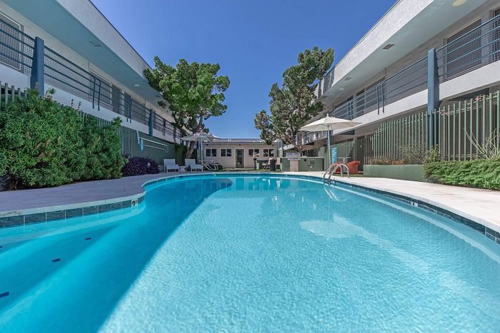 Modern apartment complex with a sparkling outdoor pool, surrounded by lush greenery and stylish lounge chairs.