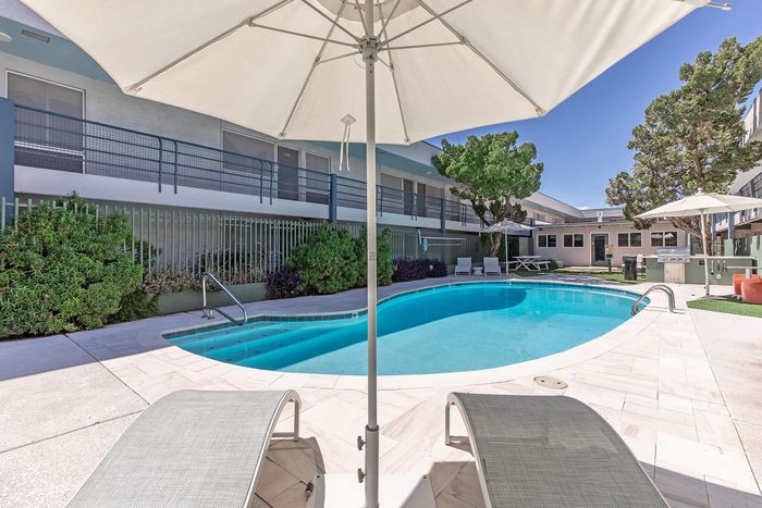 Inviting apartment pool area with sun loungers and umbrellas, surrounded by lush greenery and modern amenities for a relaxing oasis.