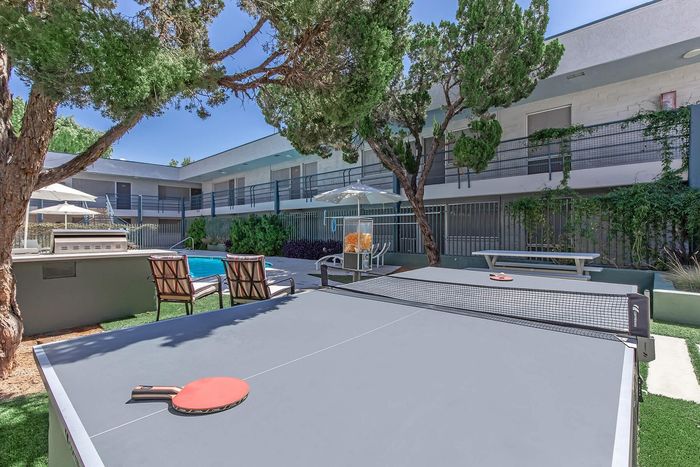 Chic apartment courtyard featuring a refreshing pool, modern lounge chairs, and a fun table tennis setup under lush green trees.