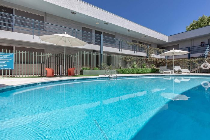 Luxurious apartment complex with a stunning outdoor pool, sun loungers, and umbrellas, perfect for relaxation and leisure.