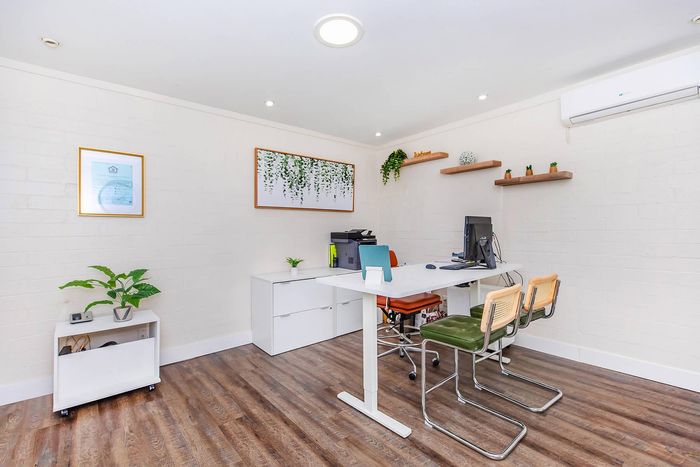 Bright and modern home office with sleek white desk, stylish shelving, and vibrant greenery, featuring elegant wooden flooring.