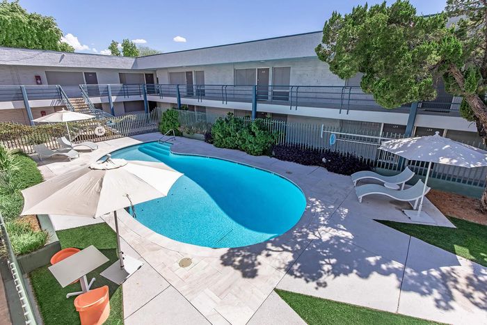 Modern apartment courtyard featuring a sparkling turquoise swimming pool surrounded by elegant lounge chairs and large umbrellas, enhancing outdoor relaxation.