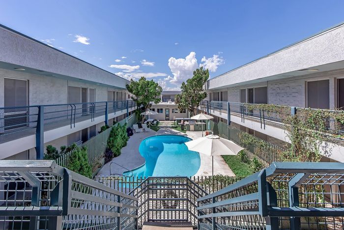 Charming apartment complex with a serene central pool, surrounded by lush greenery and modern balconies, ideal for relaxation in sunny weather.