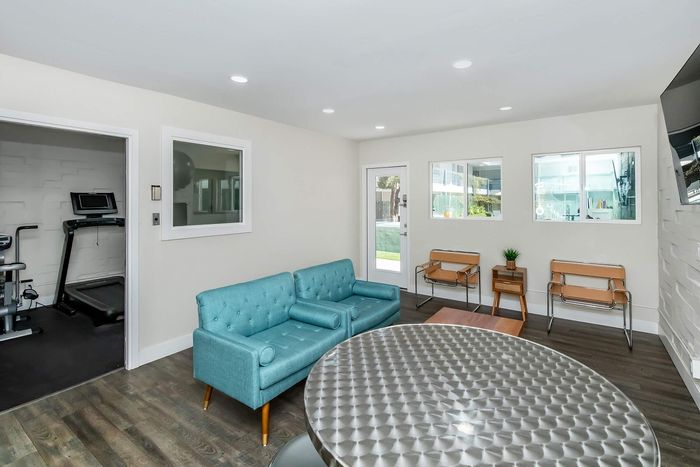 Bright and modern living area with stylish turquoise sofas, sleek metallic table, and adjacent private gym access.
