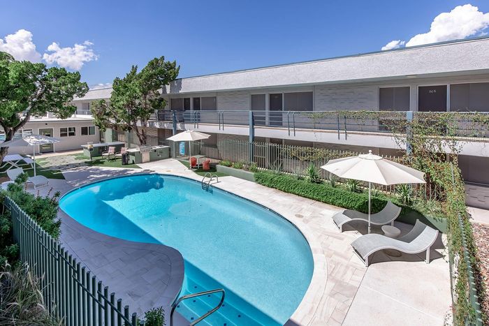 Charming outdoor oasis featuring a sparkling pool with stylish lounge chairs and shaded umbrellas, framed by lush greenery and elegant balconies.