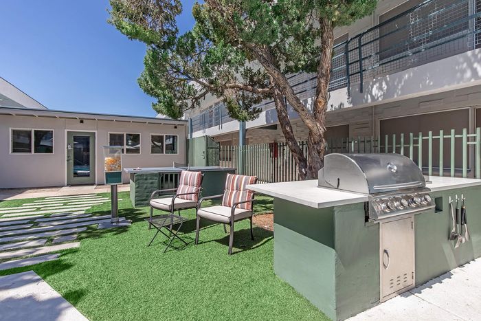 Charming outdoor space featuring a modern grill, comfortable seating, and vibrant green artificial turf, perfect for entertaining under clear blue skies.