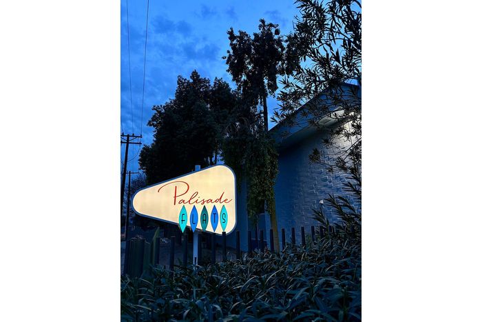 Charming evening view of Palisade Flats sign illuminated against a serene backdrop of trees and blue sky.