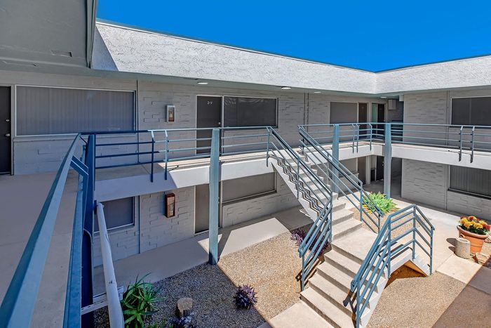 Modern apartment exterior with sleek blue railings, inviting staircases, and vibrant potted plants under a clear blue sky.
