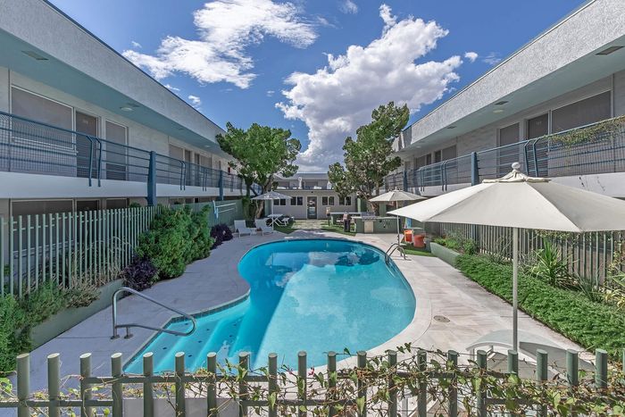 Inviting outdoor pool area surrounded by modern apartment buildings, featuring sun loungers, lush greenery, and shaded seating.