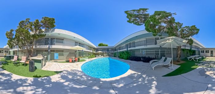 Inviting apartment complex with a sparkling outdoor pool, cozy lounging area, and lush greenery under a clear blue sky.