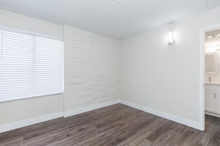 Bright, modern room with stylish wood flooring, a textured feature wall, and ample natural light from large window blinds.