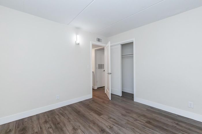 Bright and airy bedroom with sleek wooden flooring, elegant light fixture, and a spacious closet.