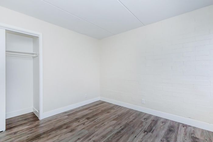 Bright, spacious room with elegant hardwood floors and a sleek open closet, perfect for a cozy apartment setting.