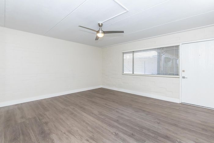 Bright and inviting living space with modern ceiling fan, sleek wooden floors, and large window for ample natural light.